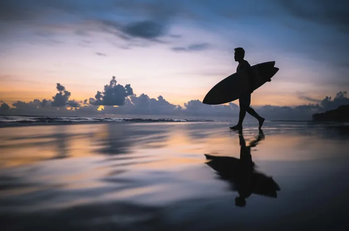 A surfer walking along the shoreline at Cox's Bazar at dusk